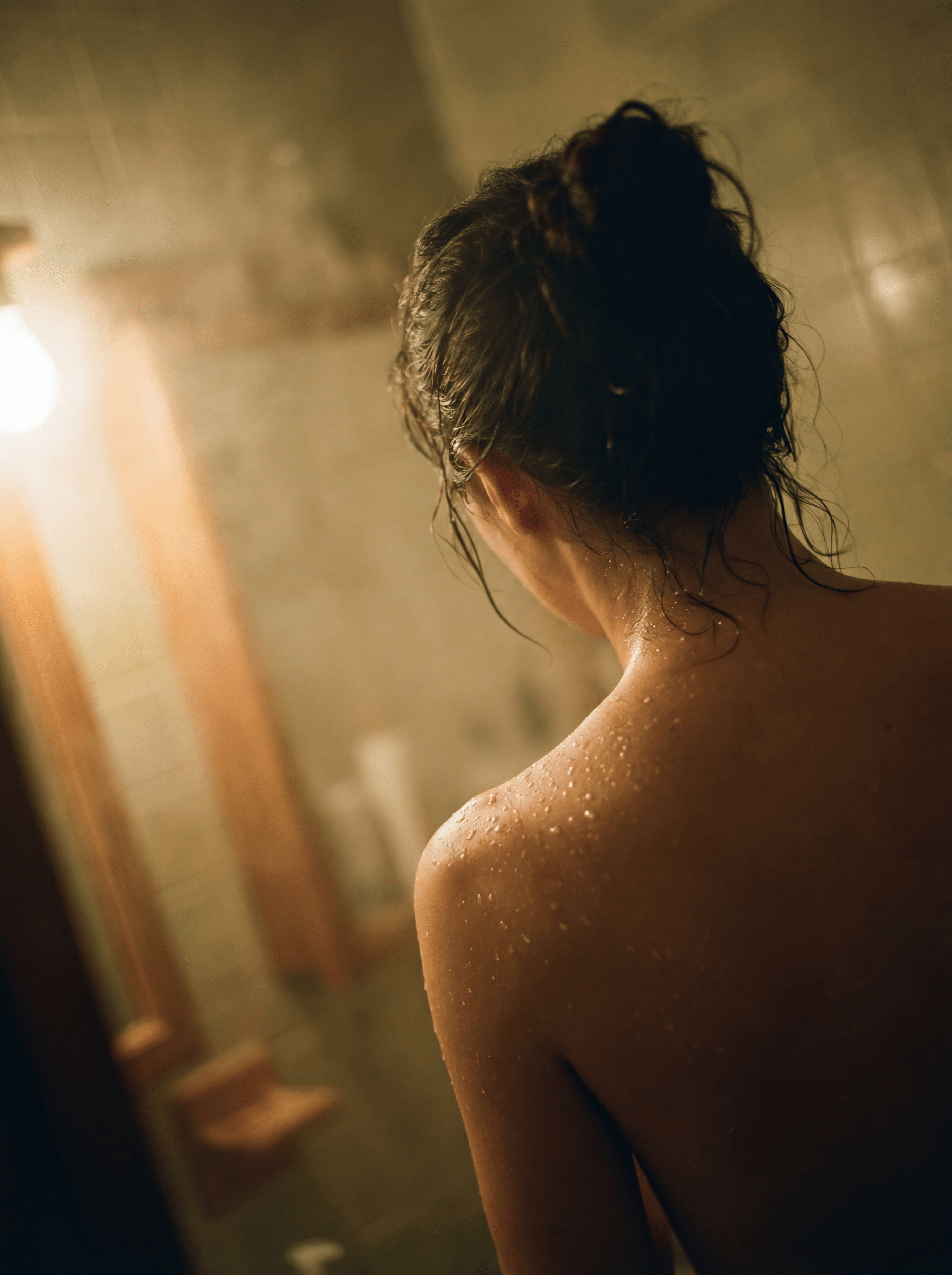 Woman's bare back with water droplets in warm steamy bathroom light